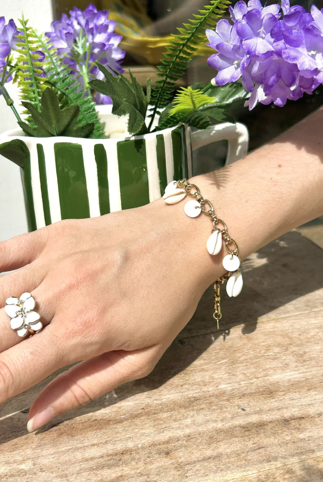 Femme portant un bracelet breloque avec petits coquillages blancs sur chaîne fine au poignet