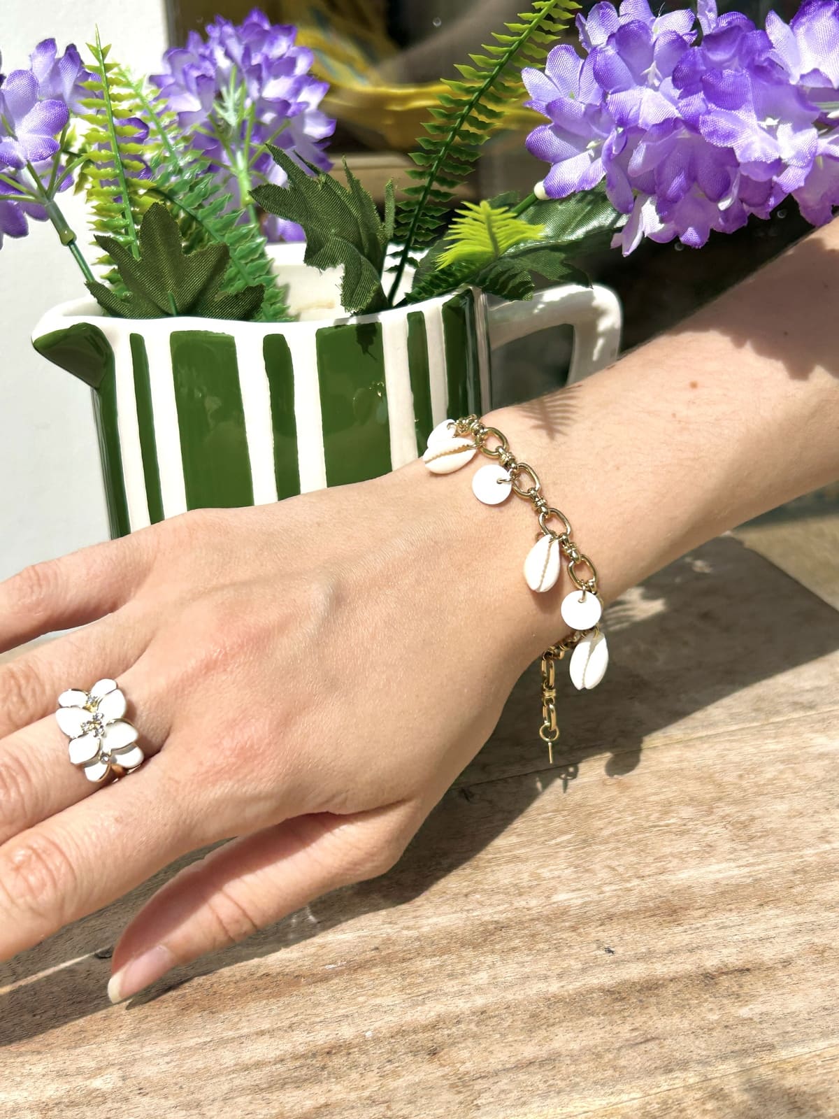 Femme portant un bracelet breloque avec petits coquillages blancs sur chaîne fine au poignet