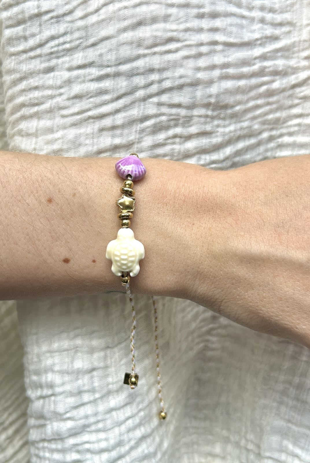 Bracelet cordon blanc avec perles tortue et coquillage porté au poignet
