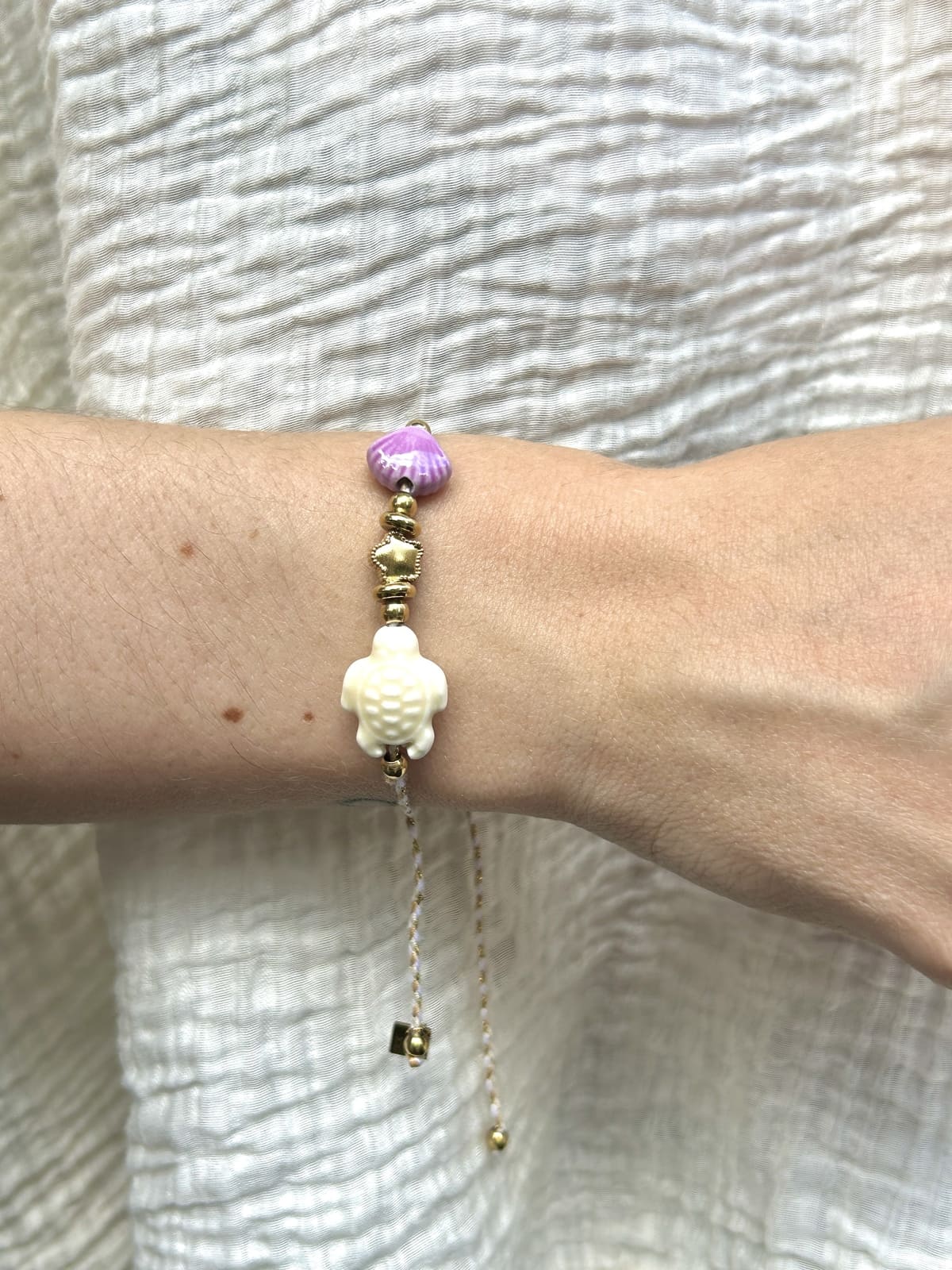 Bracelet cordon blanc avec perles tortue et coquillage porté au poignet