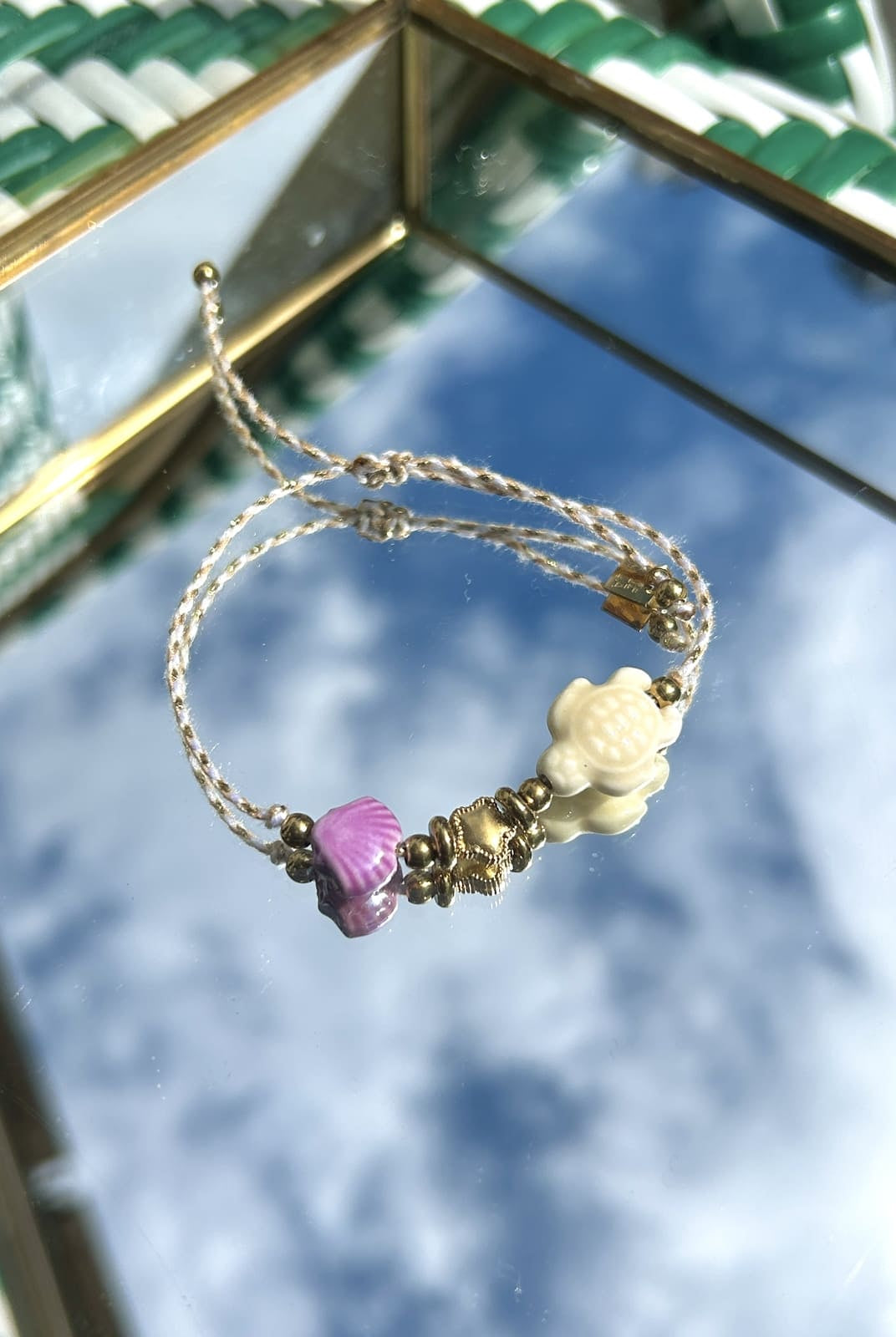 Bracelet cordon blanc avec breloques tortue et coquillage exposé sur fond neutre