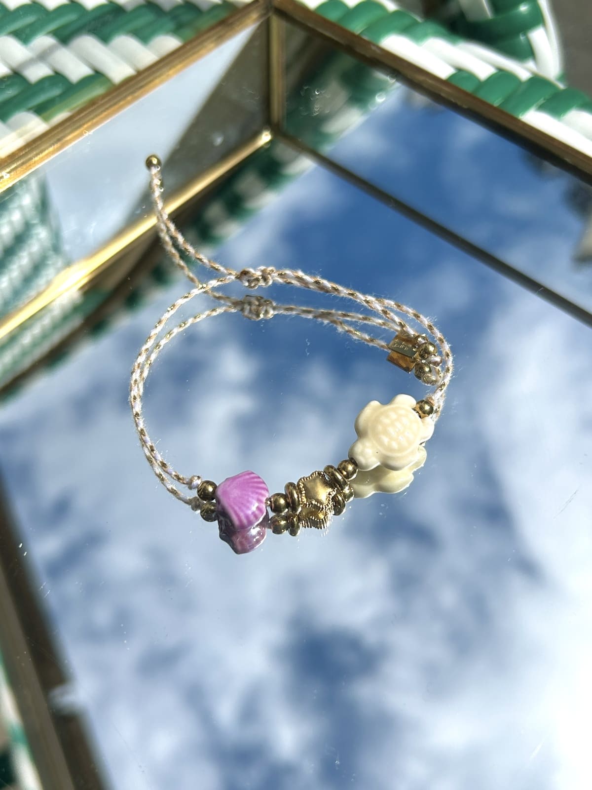 Bracelet cordon blanc avec breloques tortue et coquillage exposé sur fond neutre