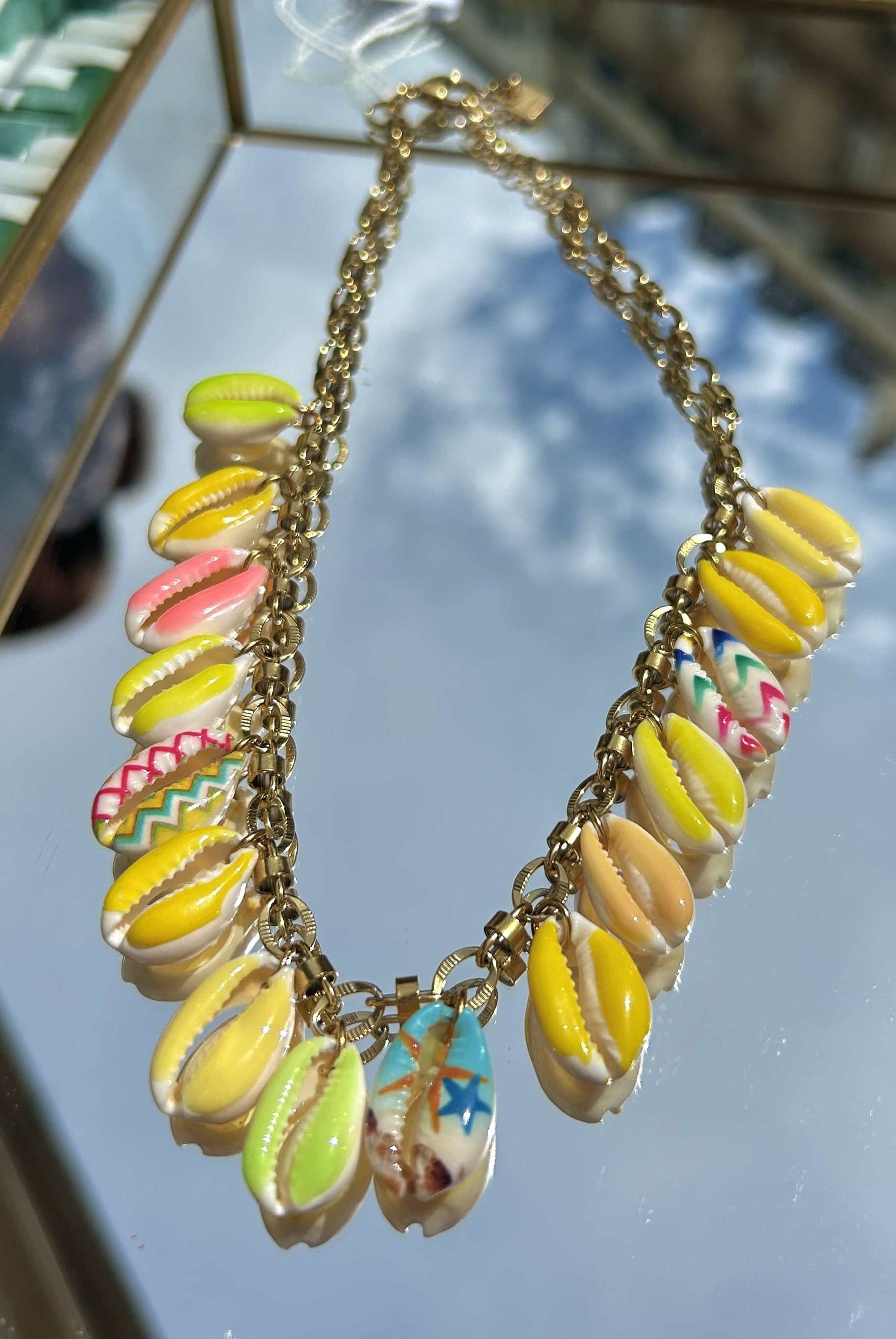 Gros plan sur les breloques coquillage jaune et rose du collier Bahia sur chaîne dorée