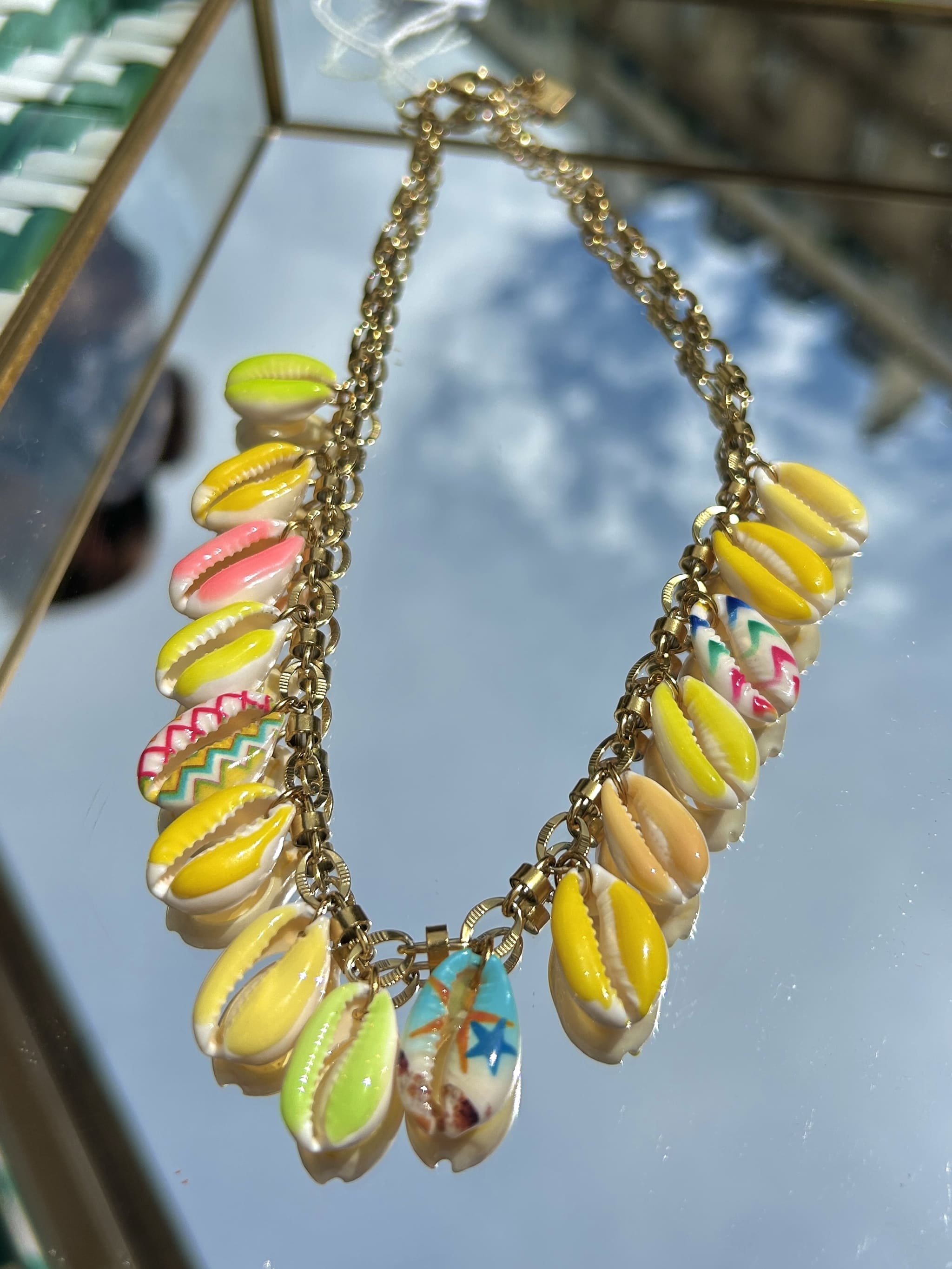 Gros plan sur les breloques coquillage jaune et rose du collier Bahia sur chaîne dorée