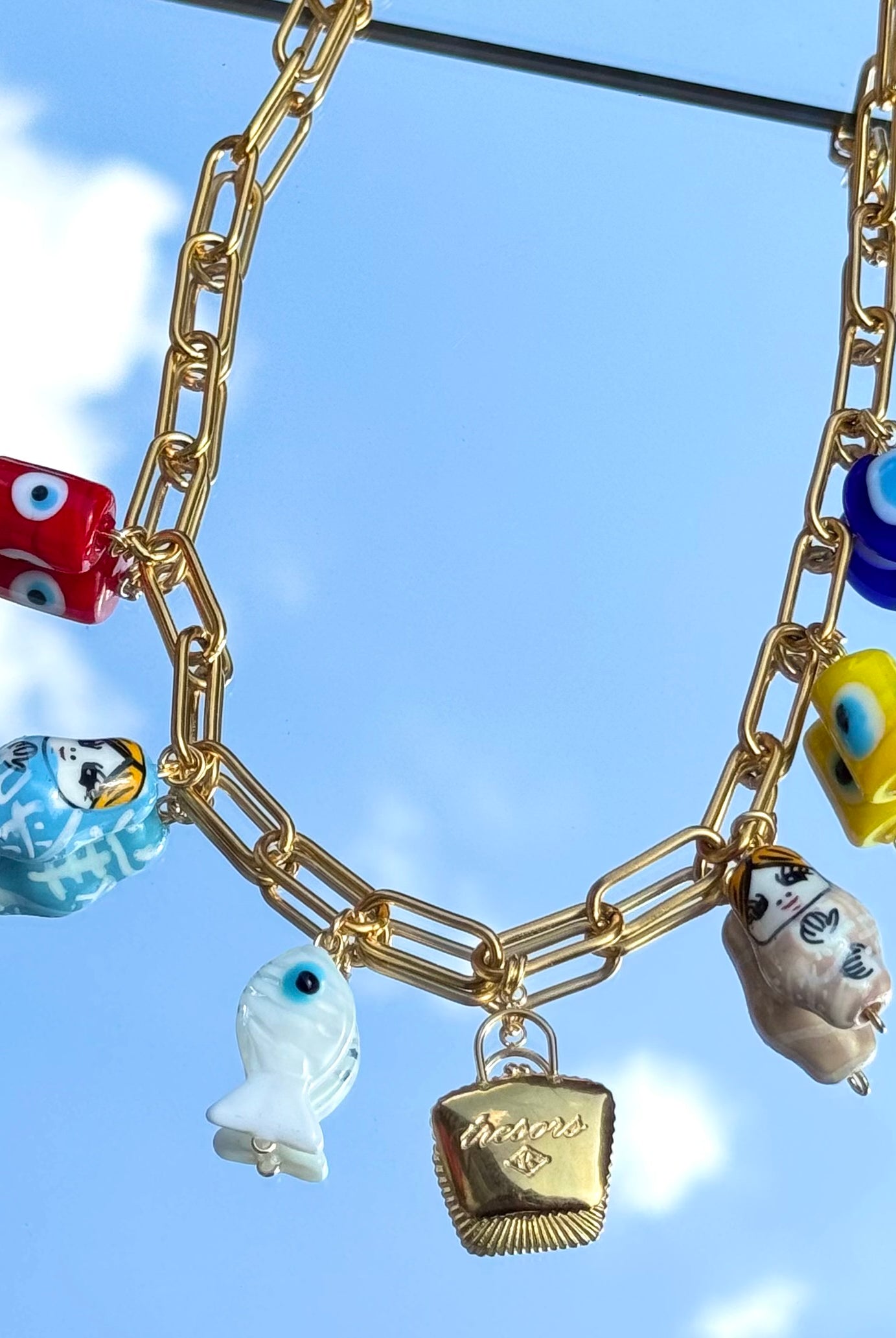 Gros plan sur les charms du collier Mamie Esther – œil grec, matriochka, sac à trésor
