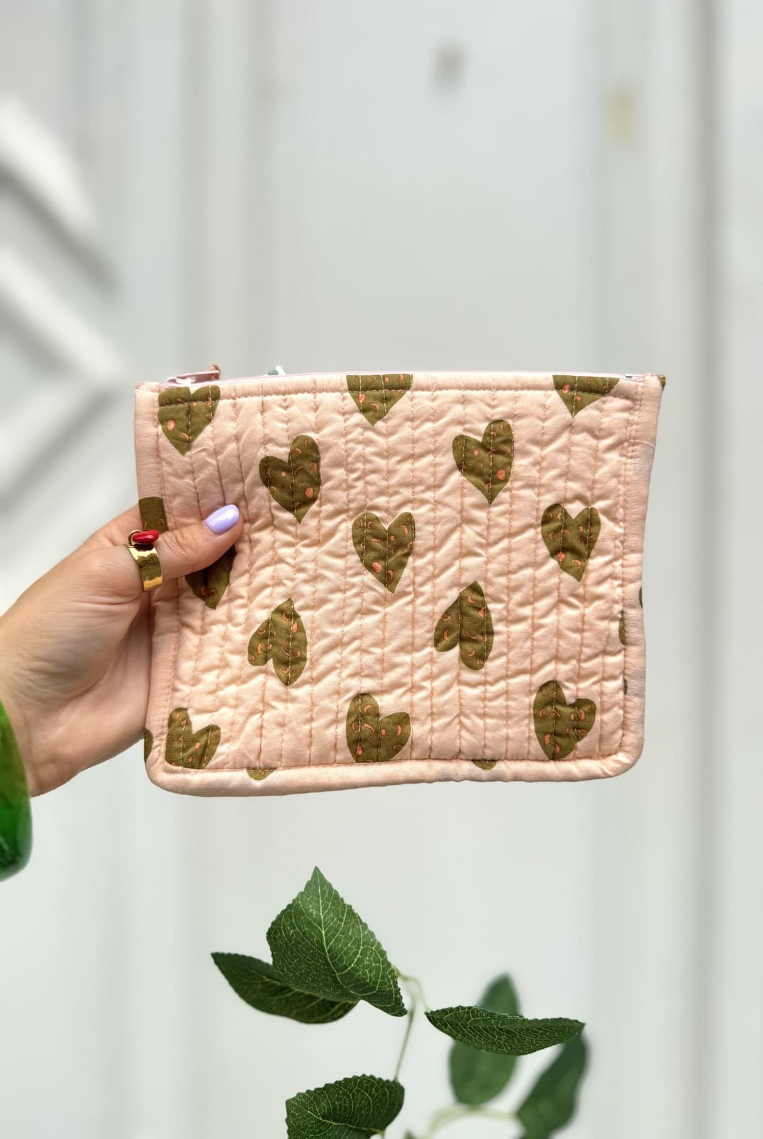 Femme présentant une pochette rose matelassée avec imprimé cœurs camel