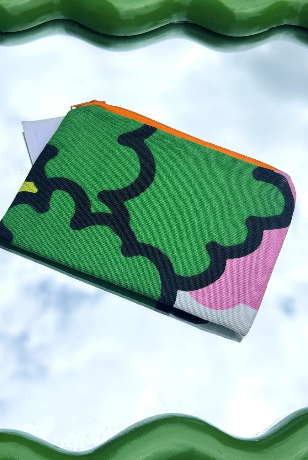 Pochette verte upcyclée posée sur un miroir vert