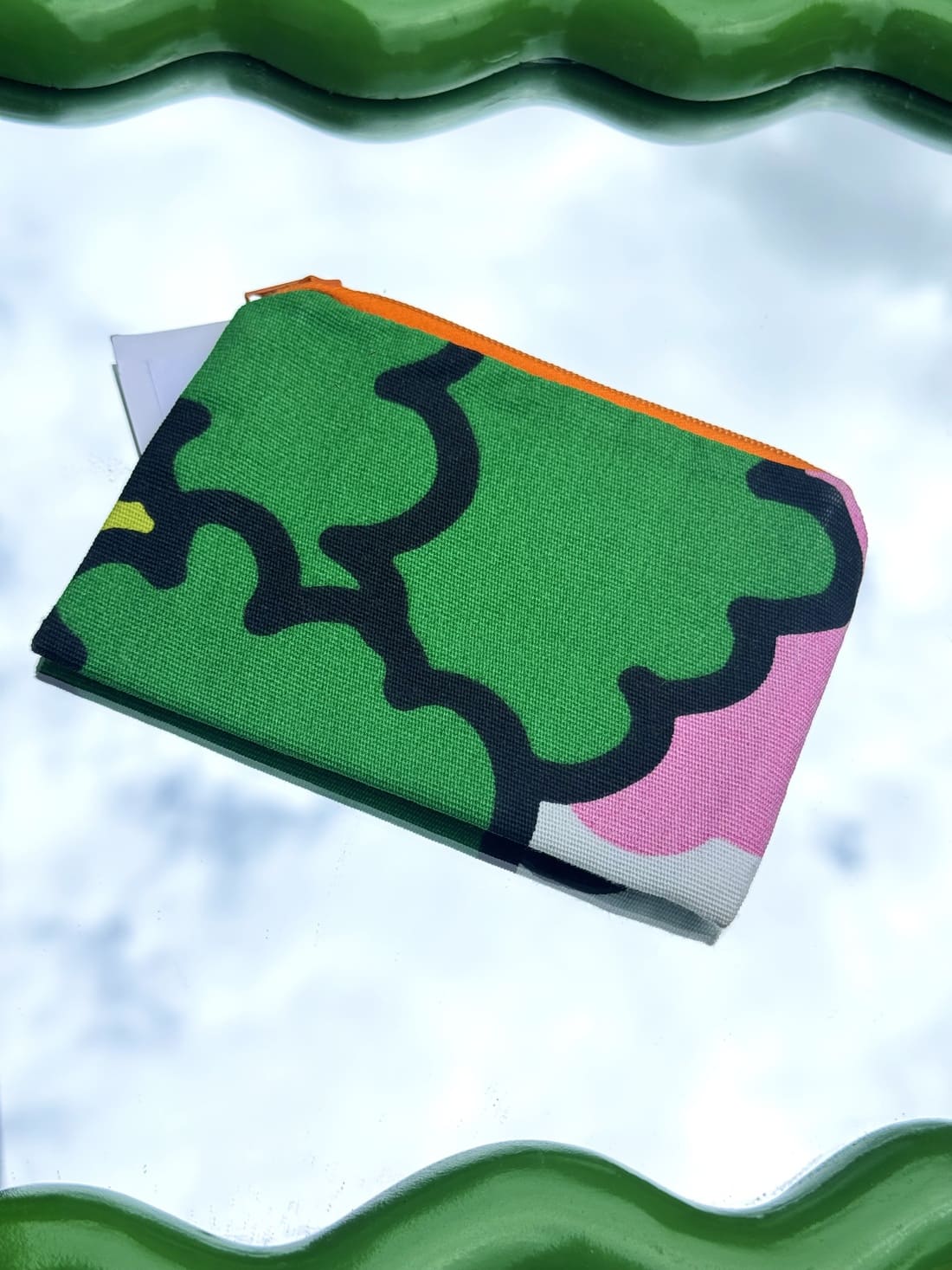 Pochette verte upcyclée posée sur un miroir vert