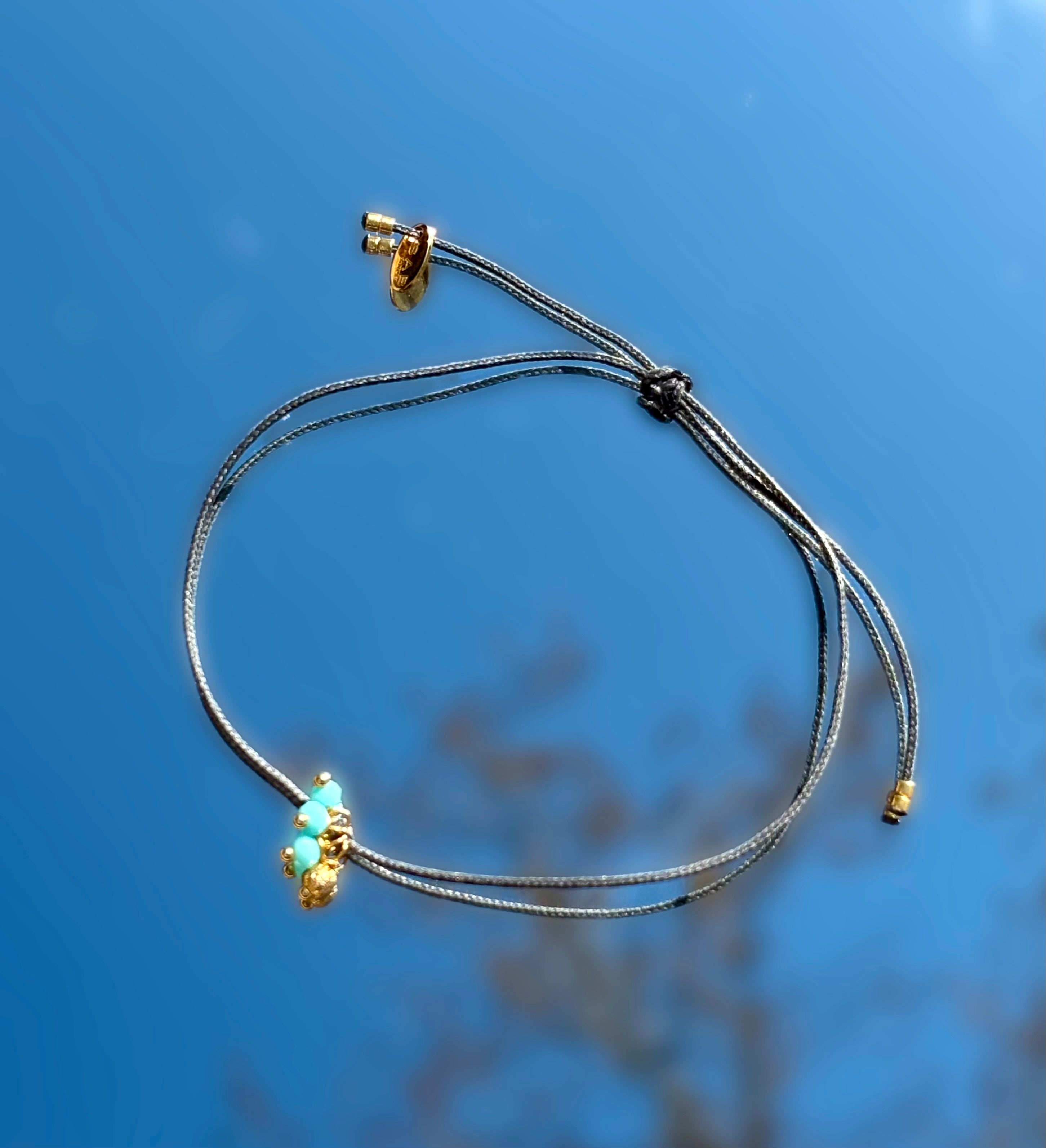 Petite perle bleu sur cordon de bracelet gris.