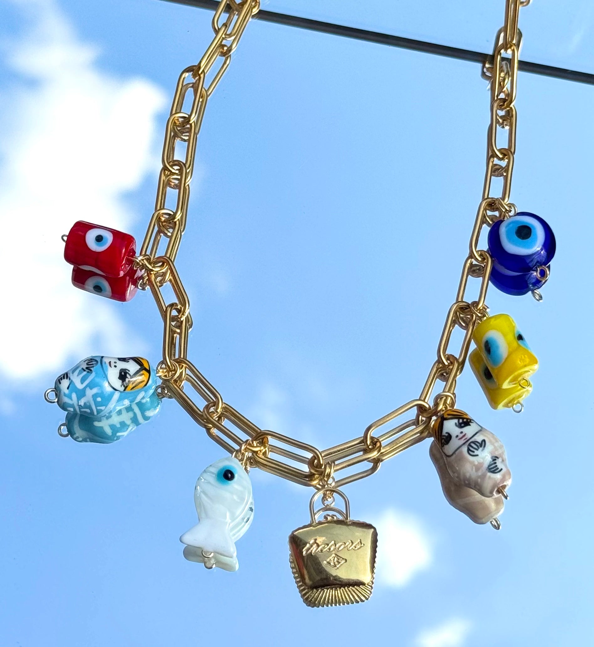 Gros plan sur les charms du collier Mamie Esther – œil grec, matriochka, sac à trésor